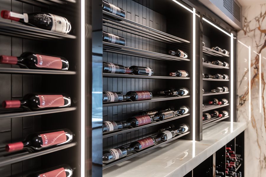 Backlit wine wall with black shelving beside a marble counter