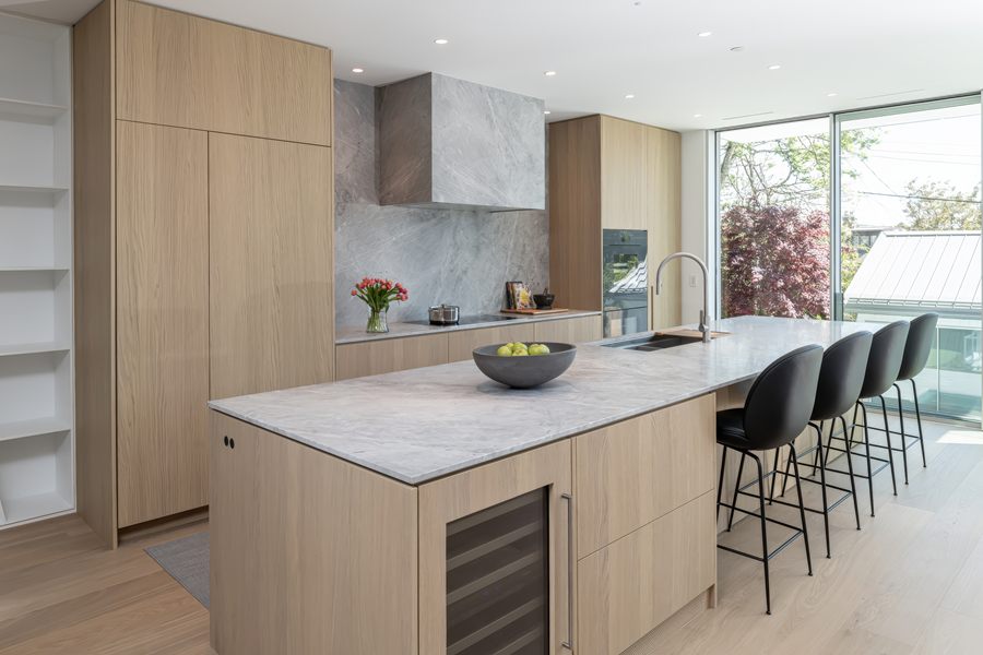 Kitchen with white oak cabinetry, a marble island and black bar stools